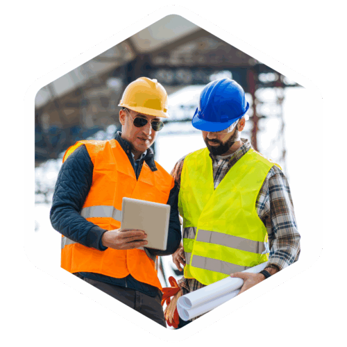 Zwei Bauarbeiter mit Schutzhelmen und Warnwesten betrachten gemeinsam ein Tablet auf einer Baustelle; einer hält zusätzlich Baupläne in der Hand.